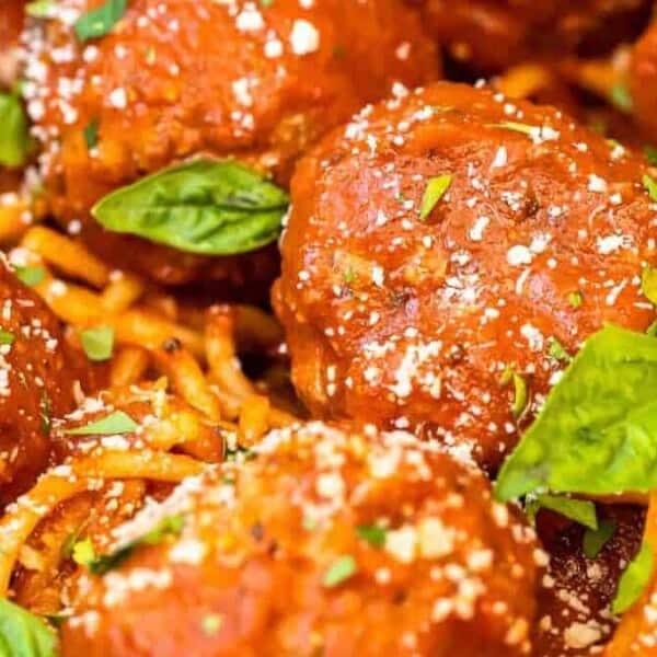 Spaghetti topped with tomato sauce, meatballs, grated cheese, and fresh basil leaves.