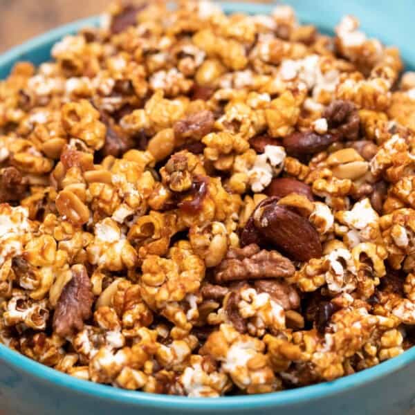 A blue bowl containing caramel-coated popcorn with almonds and pecans mixed in.