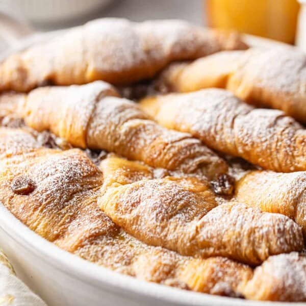 Golden croissants dusted with powdered sugar in a white dish.