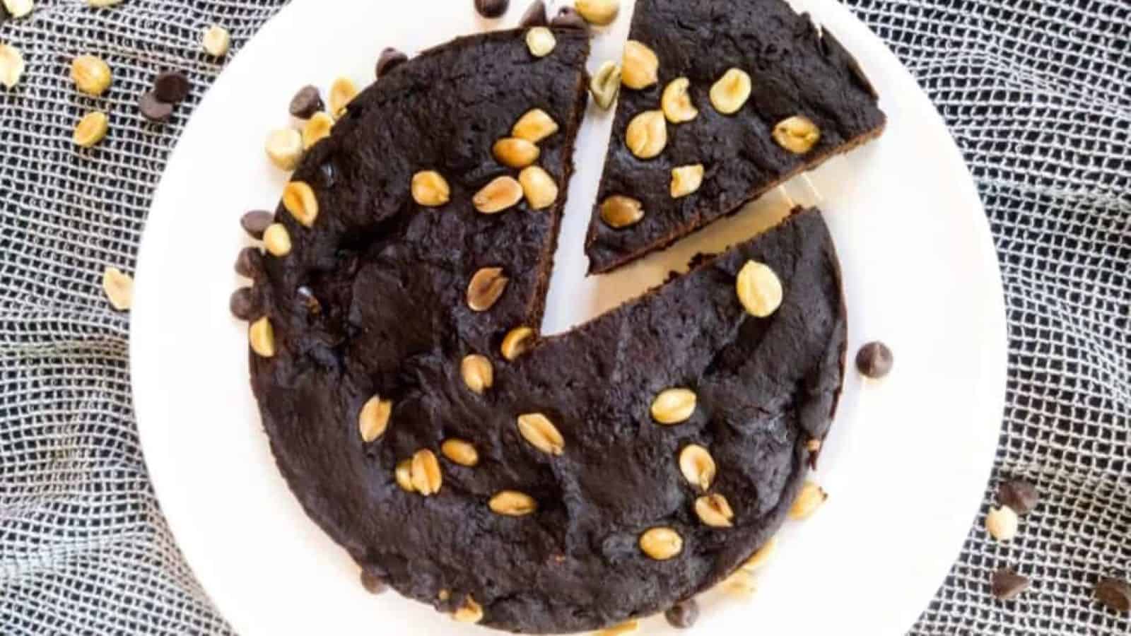 Peanut butter brownie on plate with piece cut. Chocolate chips and peanuts are on top.