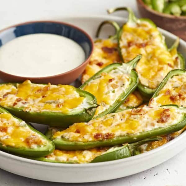 A plate of baked jalapeño poppers stuffed with cheese and bacon next to a bowl of creamy dipping sauce.