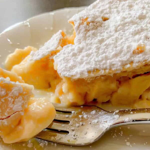 A slice of custard pie topped with powdered sugar on a white plate, with a fork holding a bite of pie.