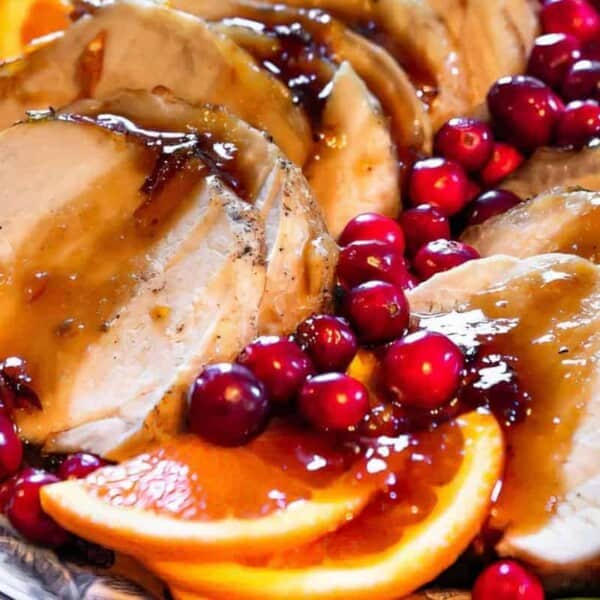 Sliced roasted turkey breast with gravy, fresh cranberries, and orange slices arranged on a serving platter.