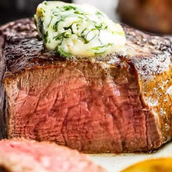 A medium-rare filet mignon with herb butter, broccoli florets, and potatoes arranged on a plate.