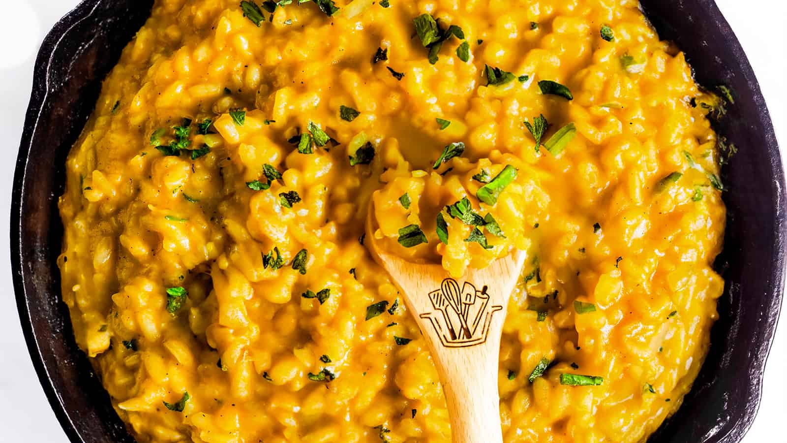 A pot of creamy yellow risotto garnished with herbs, with a wooden spoon placed in the center.