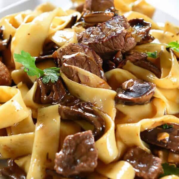 A plate of wide pasta noodles mixed with beef pieces and mushrooms, topped with parsley.