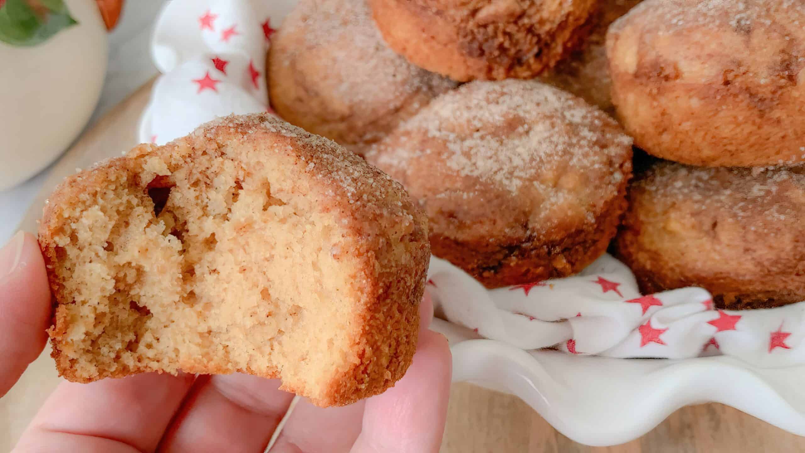 Snickerdoodle muffins with apples in dish, one with a piece out of it being held in a hand.
