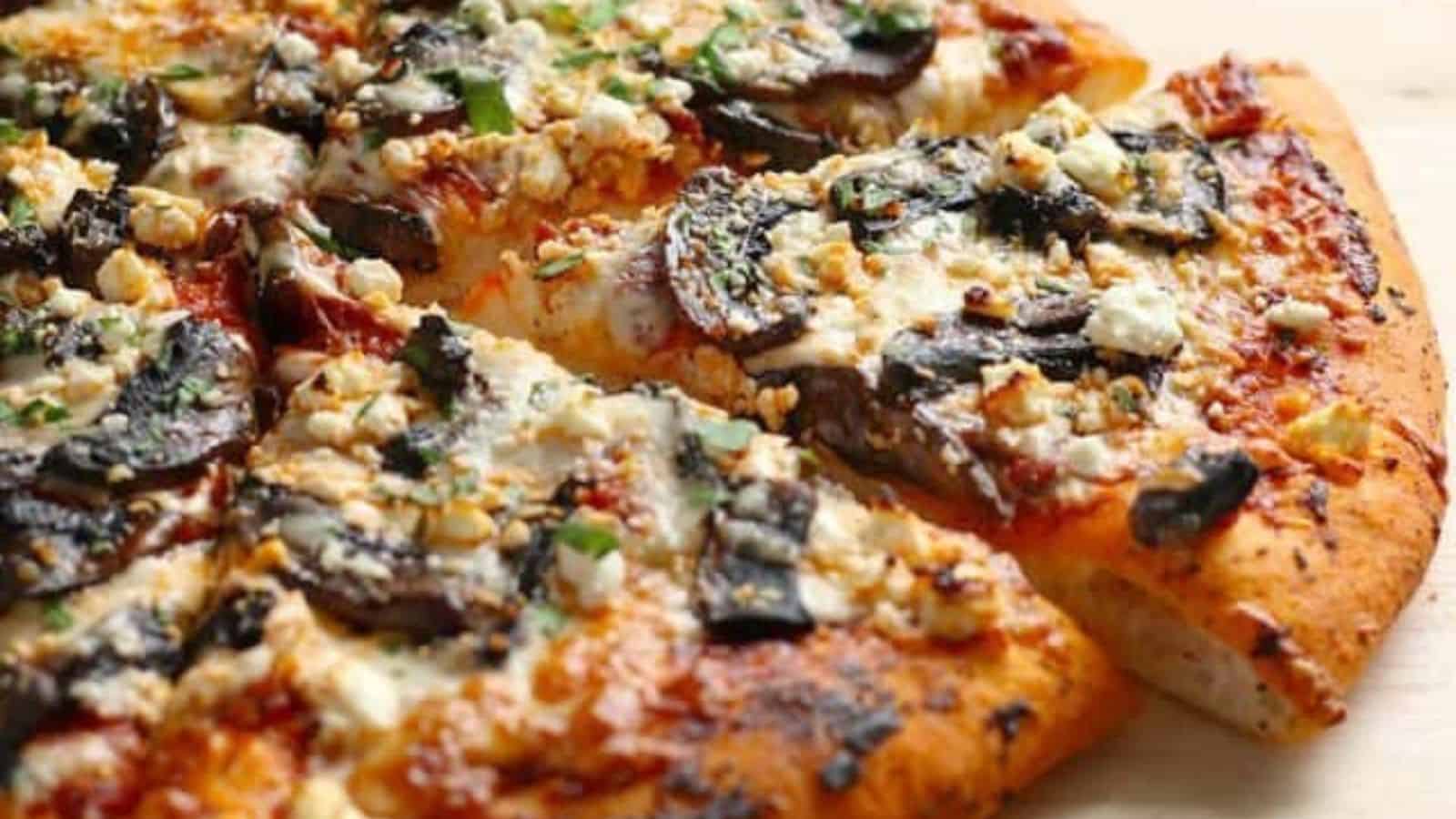 A close-up of a sliced pizza topped with mushrooms, cheese, and herbs on a wooden surface.