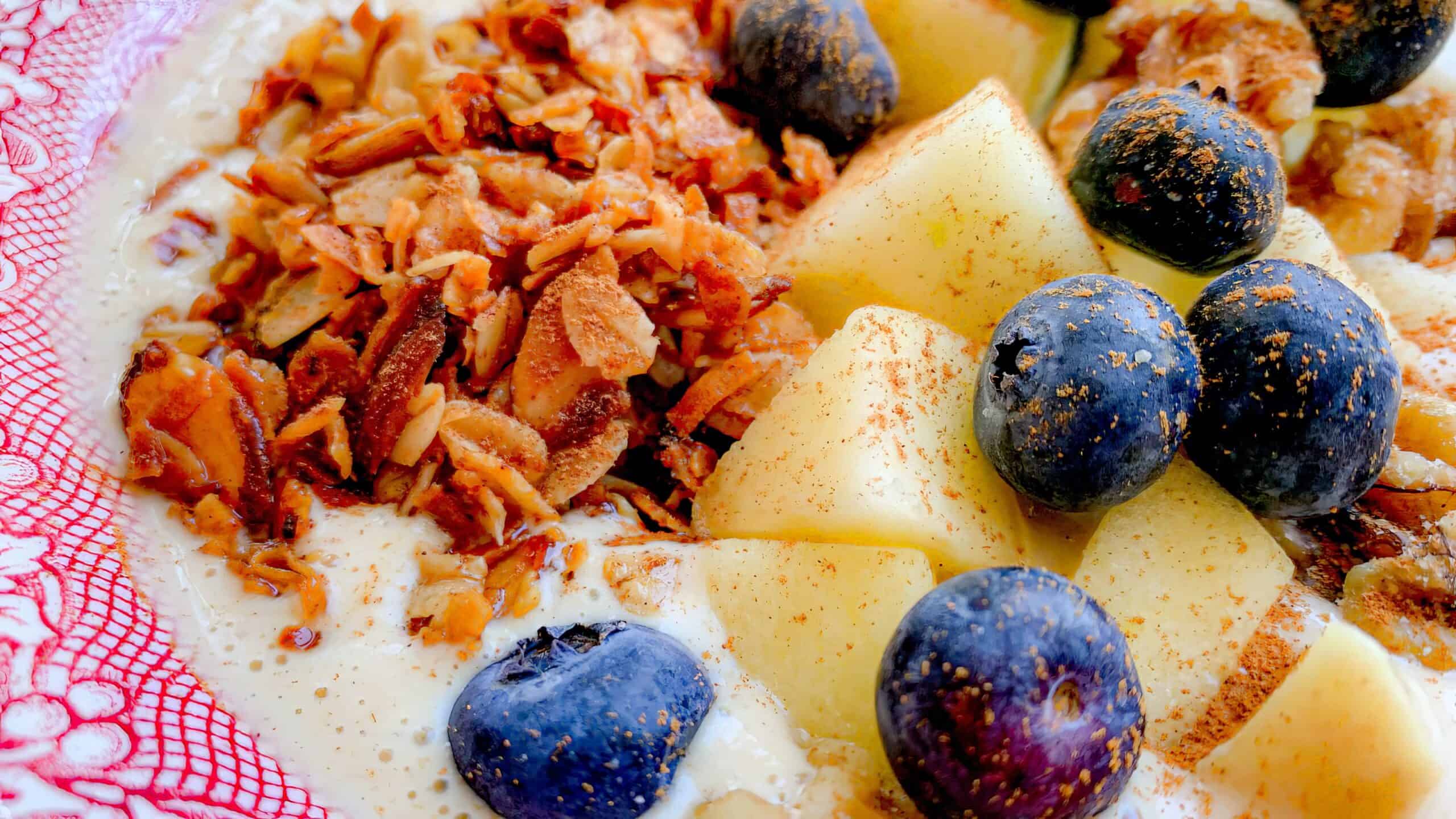 A bowl containing granola, diced apples, and blueberries in milk or yogurt with a partially visible red and white patterned edge.