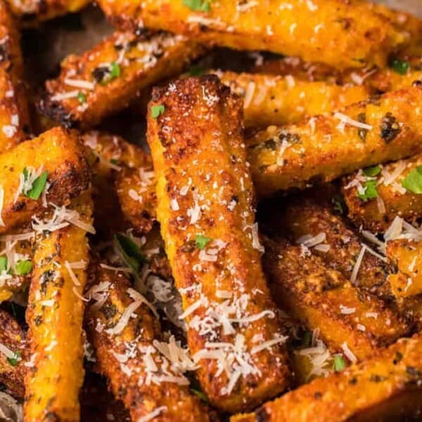 A pile of crispy, golden zucchini fries topped with grated parmesan and garnished with chopped parsley.