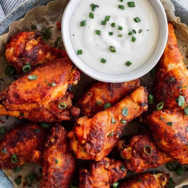 A plate of cooked chicken wings garnished with chopped green onions, accompanied by a bowl of dipping sauce.