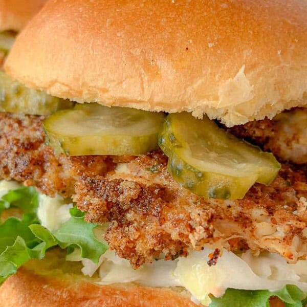 Close-up of a crispy fried chicken sandwich with lettuce, pickles, and mayonnaise on a soft bun.