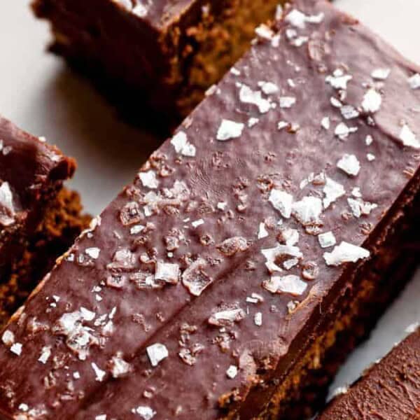 Close-up of rectangular chocolate brownies with a glossy chocolate glaze and coarse sea salt sprinkled on top.