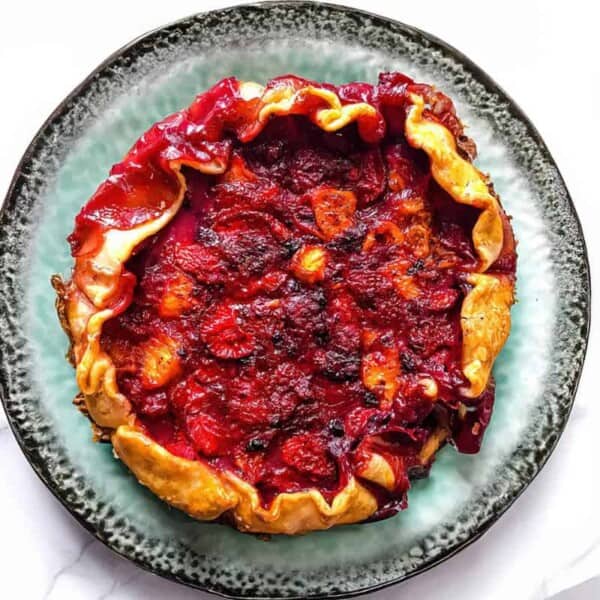 A rustic fruit galette with a golden, crimped crust and red berry filling sits on a mottled green plate.