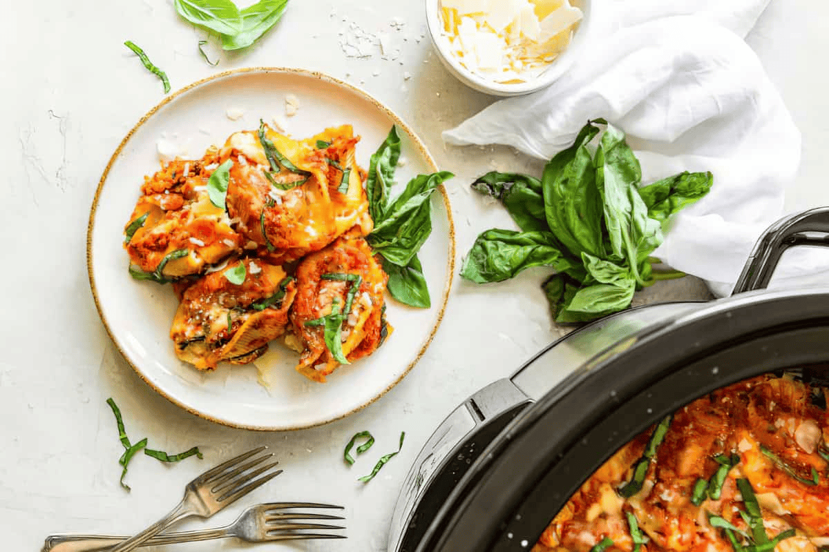 stuffed shells on plate and in slow cooker with fresh basil leaves and 2 forks.