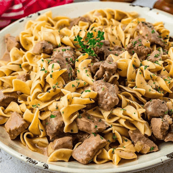 A plate of egg noodles mixed with beef chunks in creamy sauce, topped with chopped parsley.