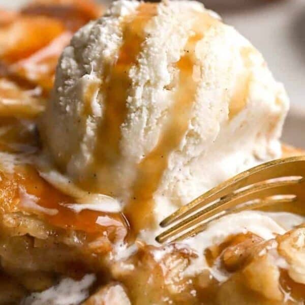 A golden fork cutting into a dessert with caramel sauce and a scoop of vanilla ice cream on a plate.