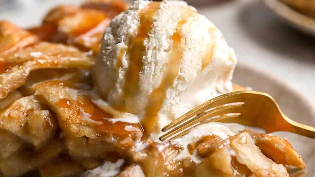 A golden fork cutting into a dessert with caramel sauce and a scoop of vanilla ice cream on a plate.