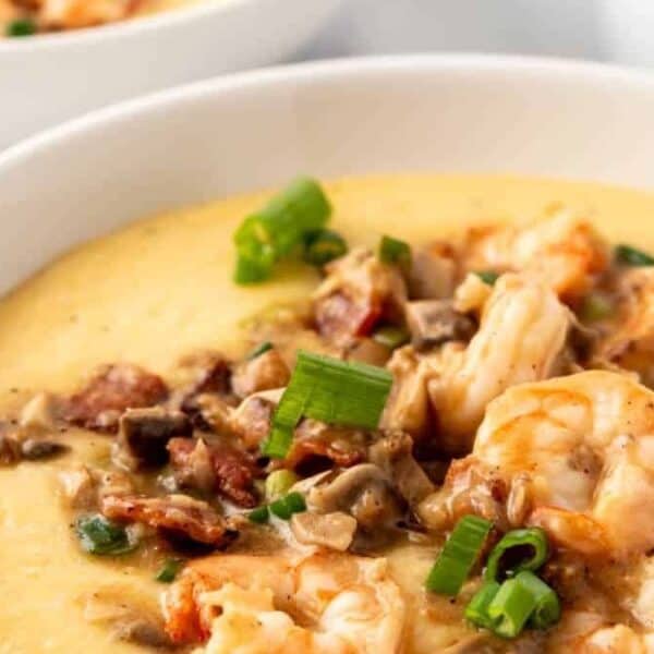 A bowl of shrimp and grits topped with chopped green onions and bacon pieces.