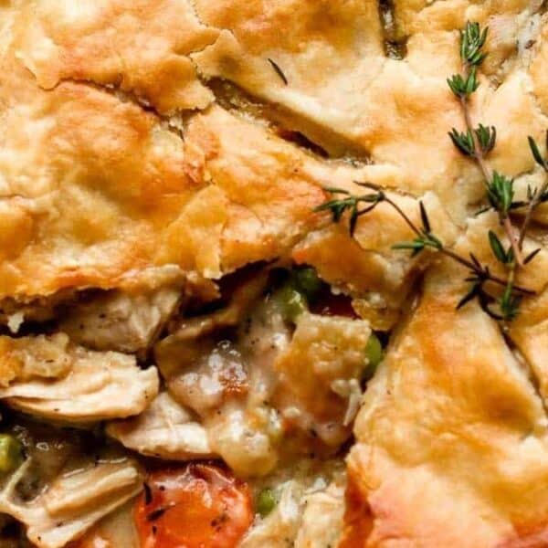 Golden-brown chicken pot pie with a slice removed, showing chicken, carrots, peas filling and sprigs of fresh thyme on top.
