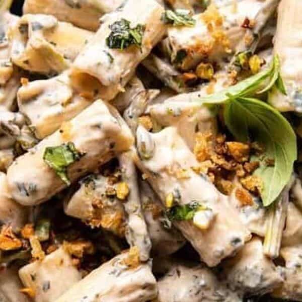 A plate of creamy rigatoni pasta topped with fresh basil leaves and crushed nuts, served with a fork.