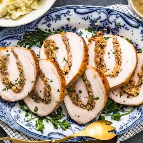 Sliced stuffed turkey breast on a blue and white platter, with mashed potatoes and gravy visible in the background.