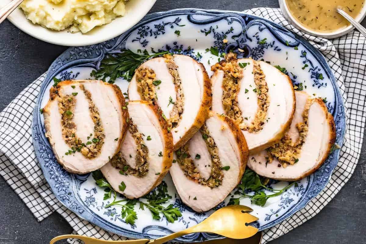 Sliced stuffed turkey breast on a blue and white platter, with mashed potatoes and gravy visible in the background.