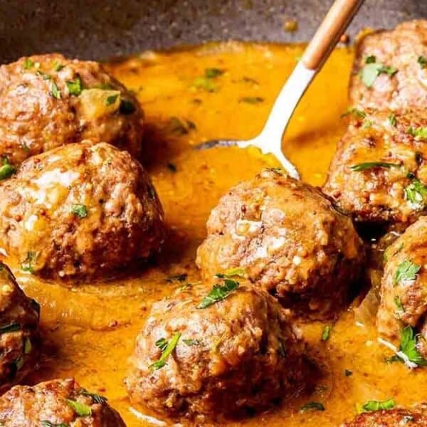 Ground beef meatballs in brown sauce, topped with herbs, presented in a skillet alongside a serving spoon.