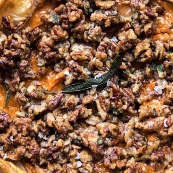 A baked tart with a golden crust, orange filling, topped with chopped pecans and garnished with a fresh sage leaf.