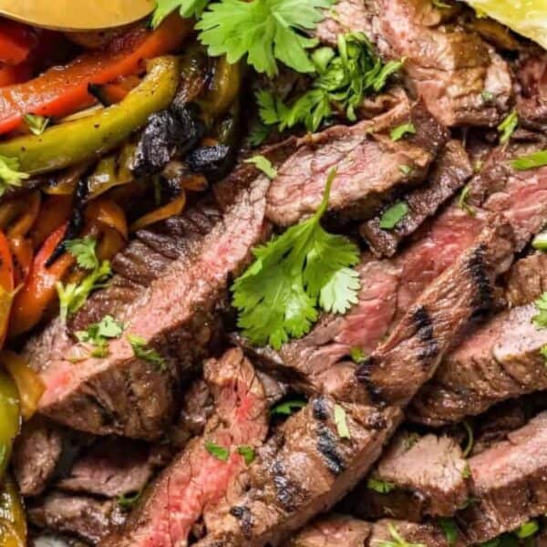 Sliced grilled steak topped with cilantro and lime, accompanied by sautéed bell peppers.