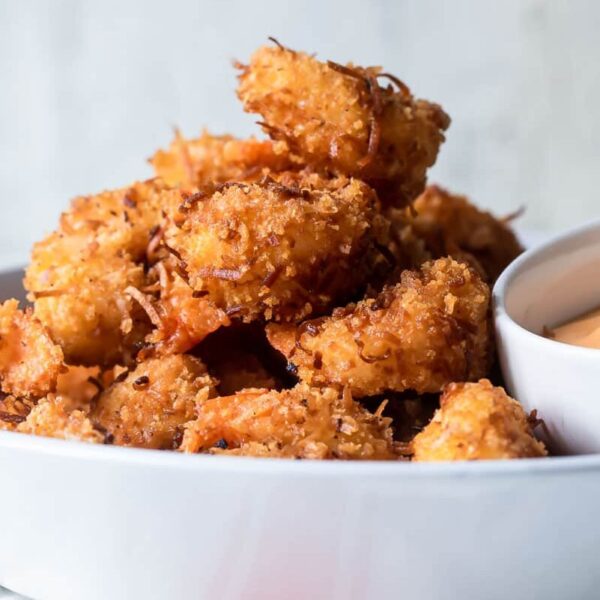 A white dish filled with crispy breaded shrimp beside a small bowl of orange dipping sauce.