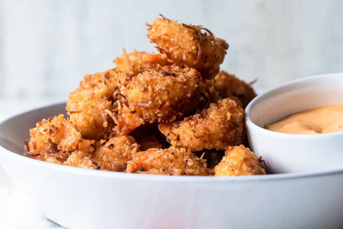 A white dish filled with crispy breaded shrimp beside a small bowl of orange dipping sauce.