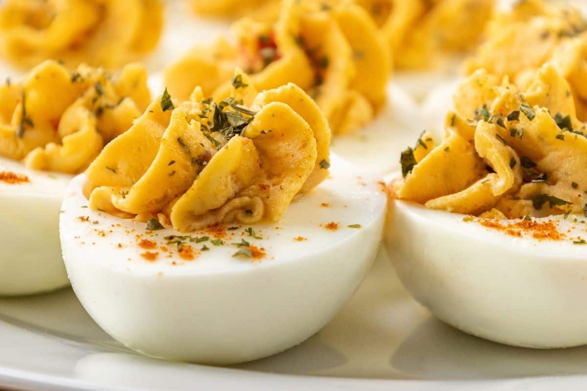 Close-up of deviled eggs garnished with herbs and paprika, arranged on a white plate.