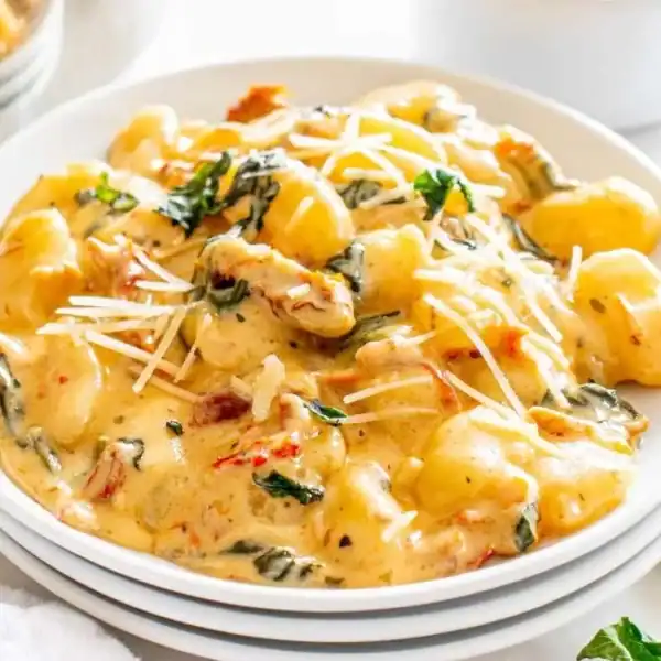 A plate of creamy gnocchi topped with grated cheese and garnished with fresh basil, placed on a white table next to a fork.