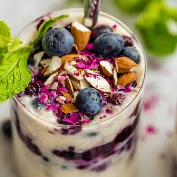 A glass filled with layered yogurt, blueberries, chopped almonds, and grated beets, garnished with a sprig of mint.
