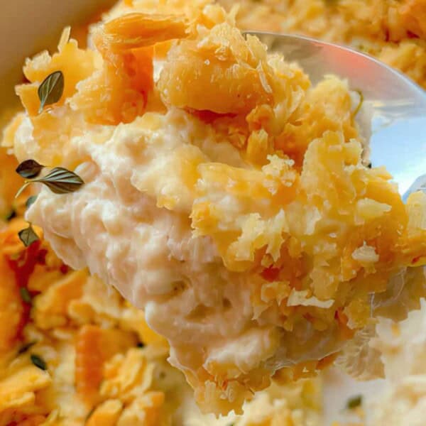 A close-up of a spoonful of creamy casserole topped with crushed crackers and herbs, held above a serving dish.