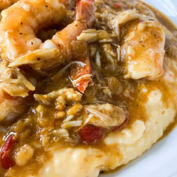 A plate of creamy mashed potatoes topped with succulent shrimp and a rich, savory gravy. The dish is garnished with chunks of crab meat and small pieces of red bell pepper, adding color and texture to the meal. The gravy glistens, blending the flavors together.