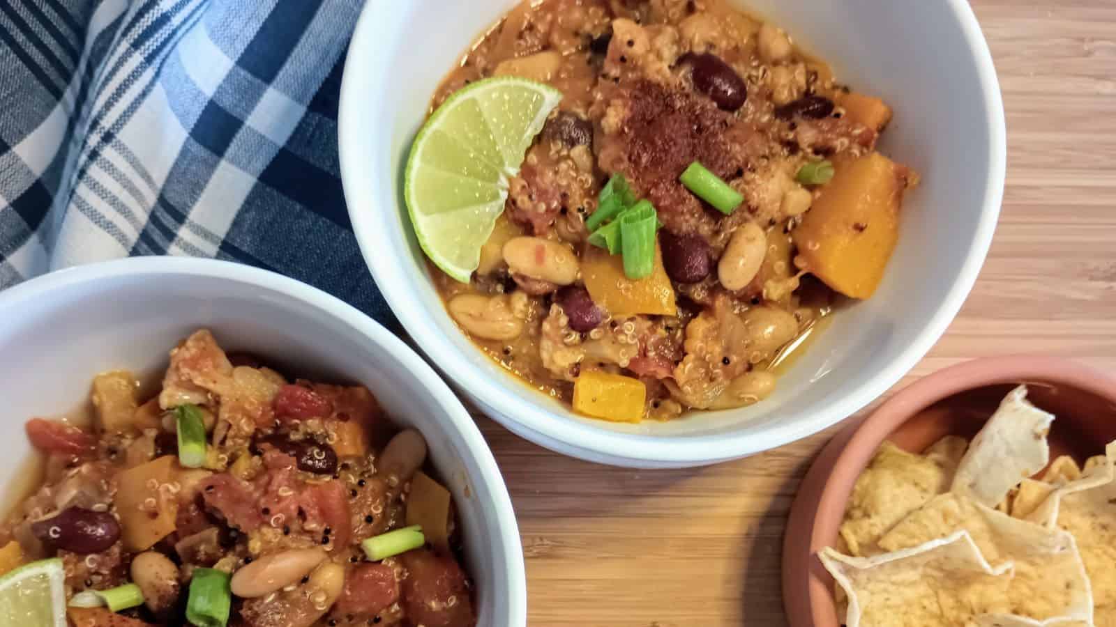 2 bowls of vegetarian chili with butternut squash and cauliflower next to bowl of tortilla chips.