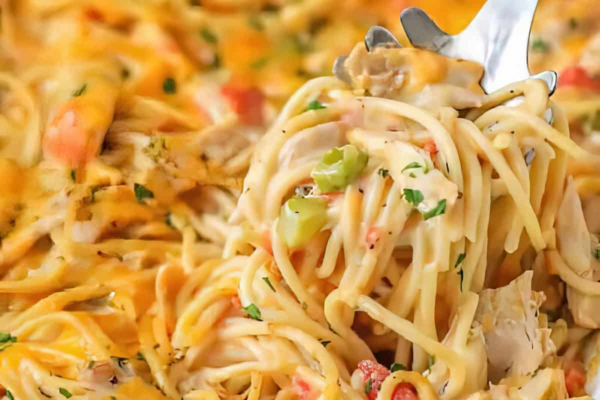 Close-up of a fork lifting a serving of creamy spaghetti, garnished with herbs and mixed with vegetables. The pasta appears rich and cheesy, creating a warm and appetizing presentation.