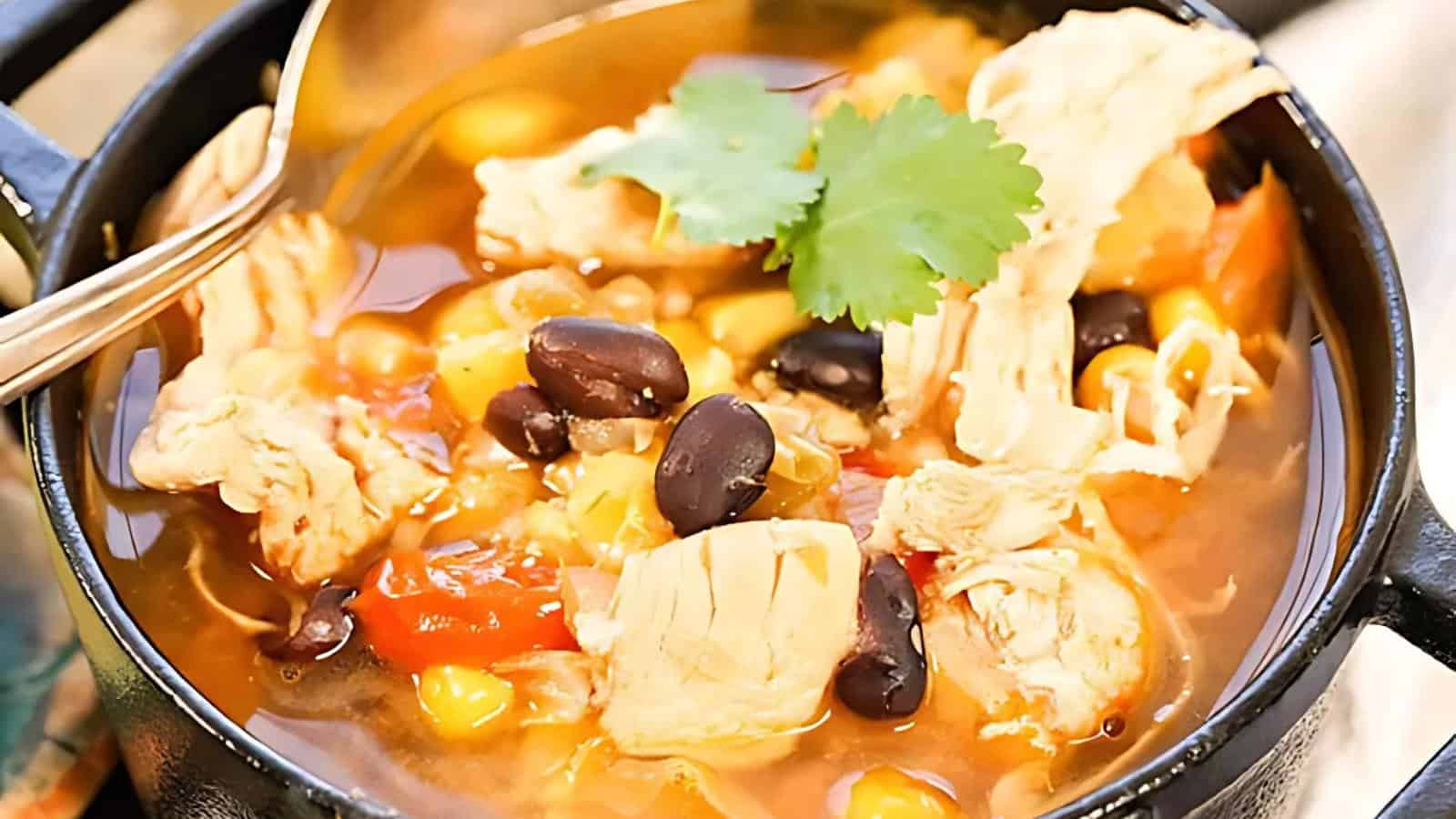 A bowl of chicken soup containing black beans, corn, tomatoes, and a cilantro garnish.