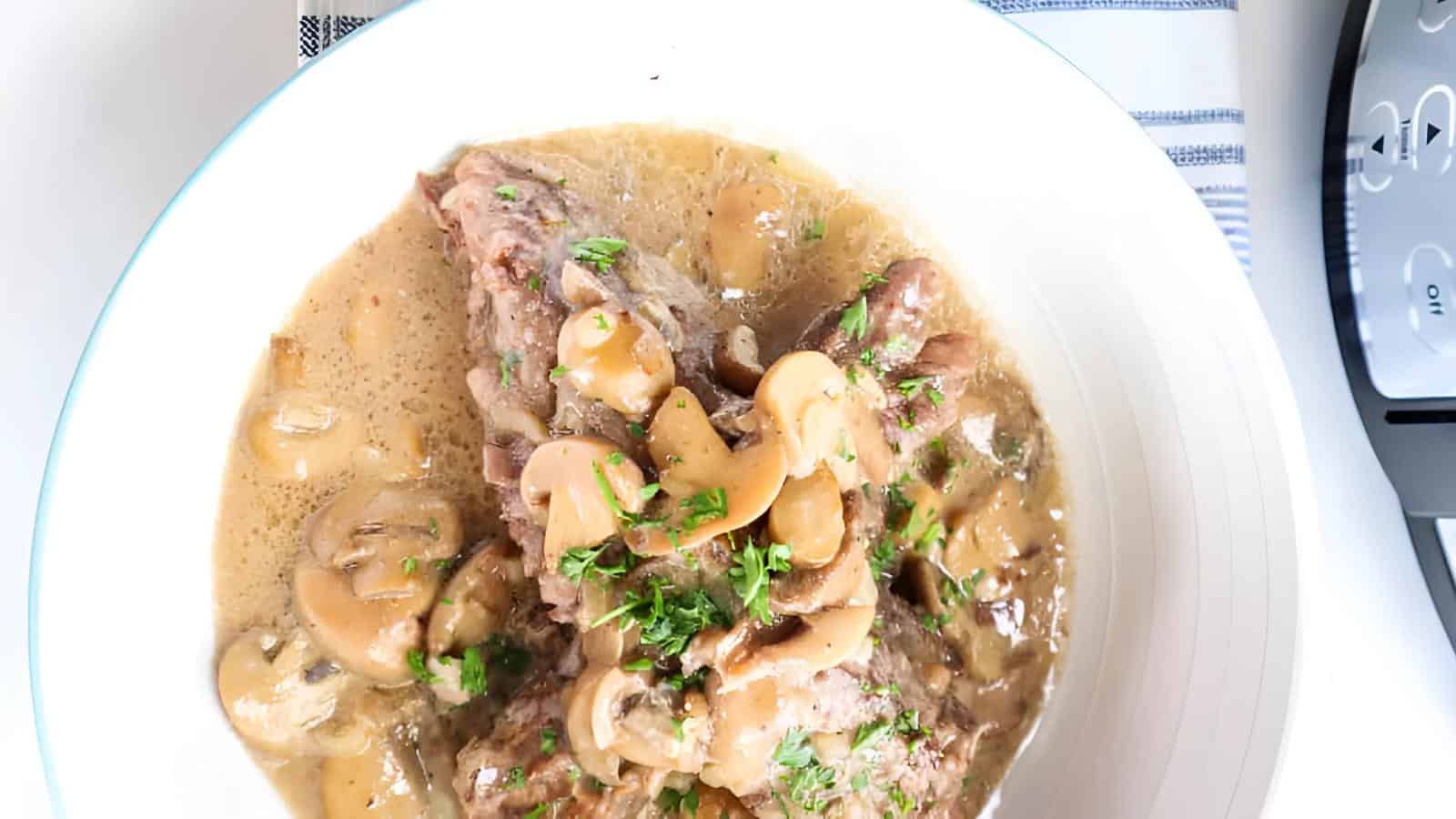 A white plate with beef stroganoff featuring mushrooms, parsley, and creamy sauce.