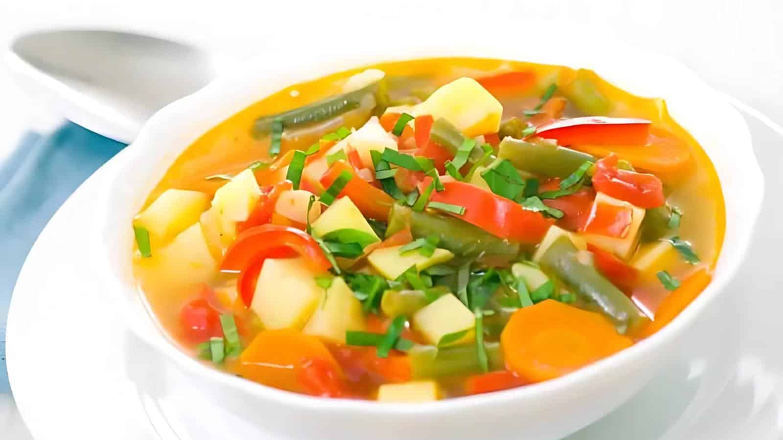 A bowl containing carrots, green beans, potatoes, and chopped herbs is served in a white dish with a spoon nearby.