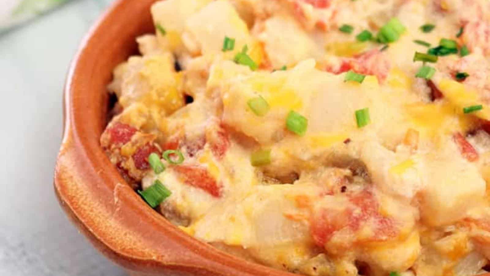 A ceramic dish containing a casserole topped with melted cheese, slices of tomato, and a sprinkle of chopped green onions.