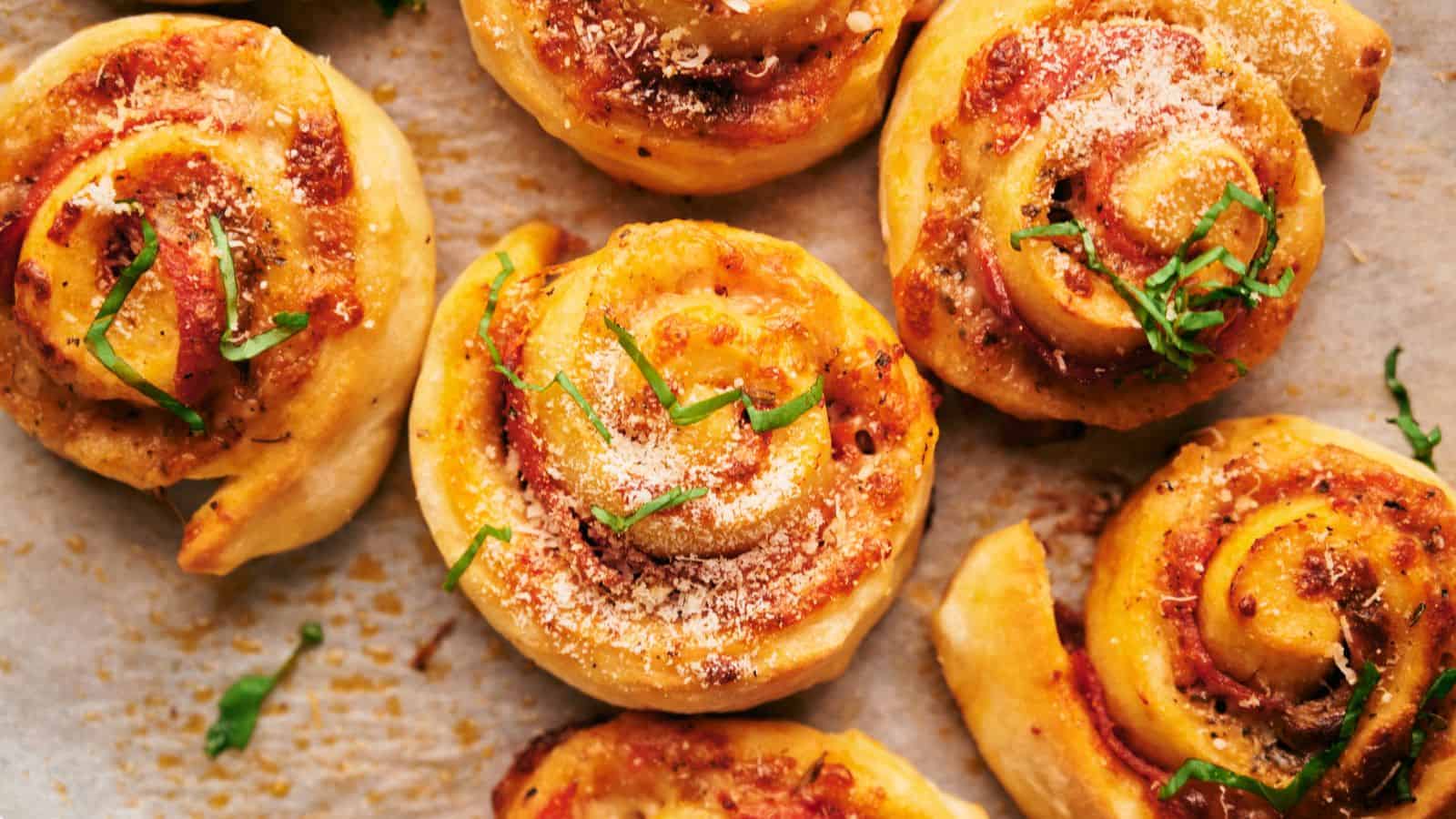 Close-up of freshly baked pizza rolls topped with grated cheese and garnished with fresh basil leaves on a parchment-lined surface.
