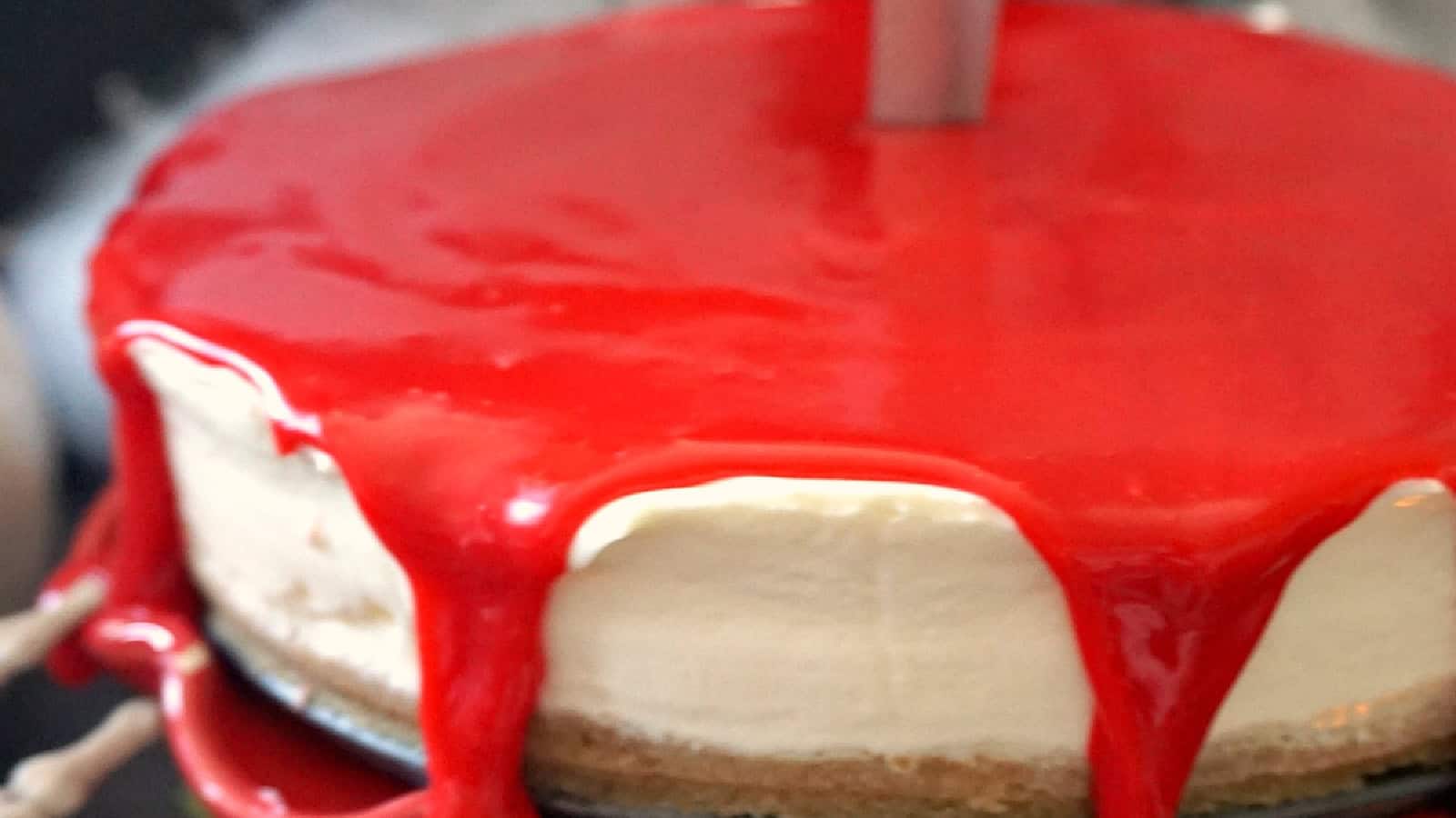 A creamy cheesecake with bright red glaze dripping down the sides.