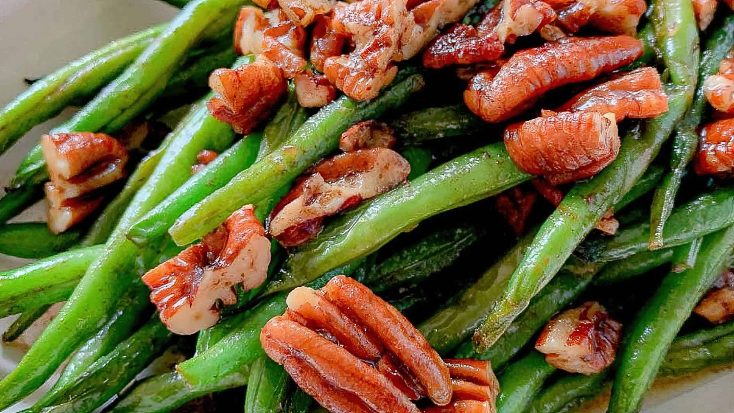 A close-up of a dish featuring cooked green beans topped with roasted pecan pieces. The vibrant green beans are glossy, and the pecans add a touch of brown, creating a visually appealing contrast.