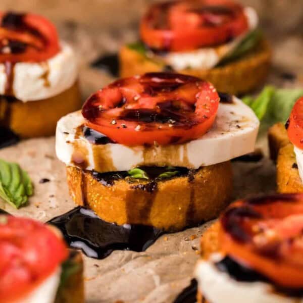 Toasted bread slices with fresh mozzarella, tomato, basil, and balsamic glaze on top, set on a baking sheet.