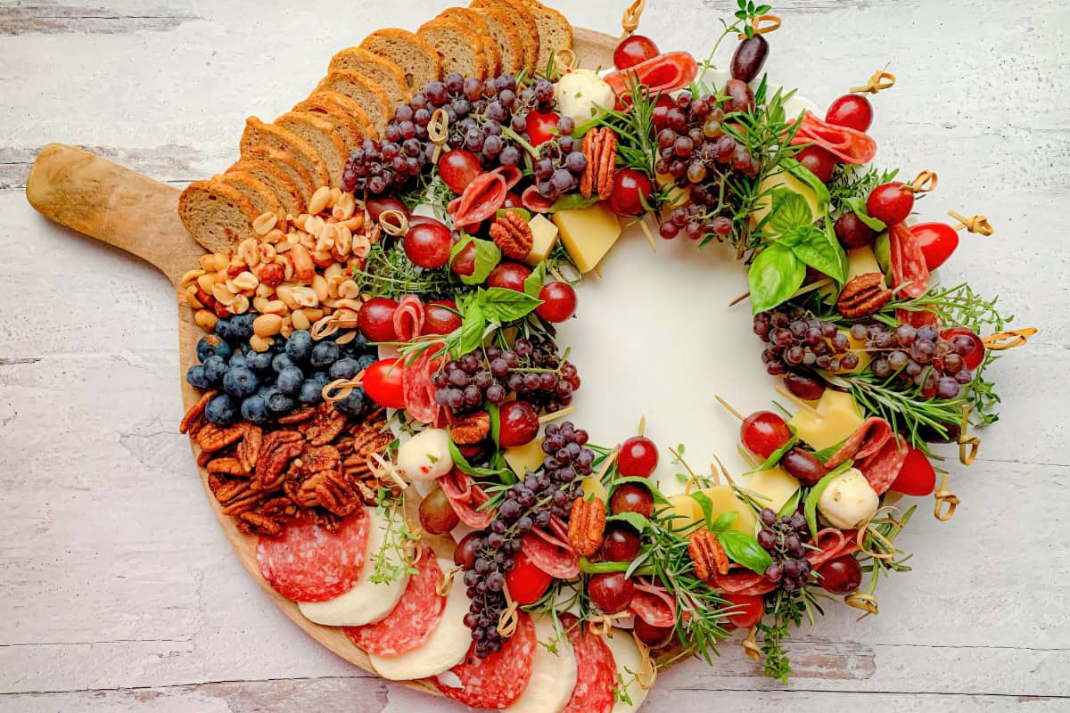Circular charcuterie board featuring assorted meats, cheeses, grapes, nuts, blueberries, and greens on a wooden surface.