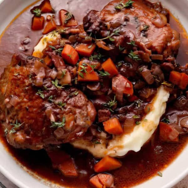 Braised meat with carrots and herbs over mashed potatoes, topped with brown sauce, served in a white bowl.