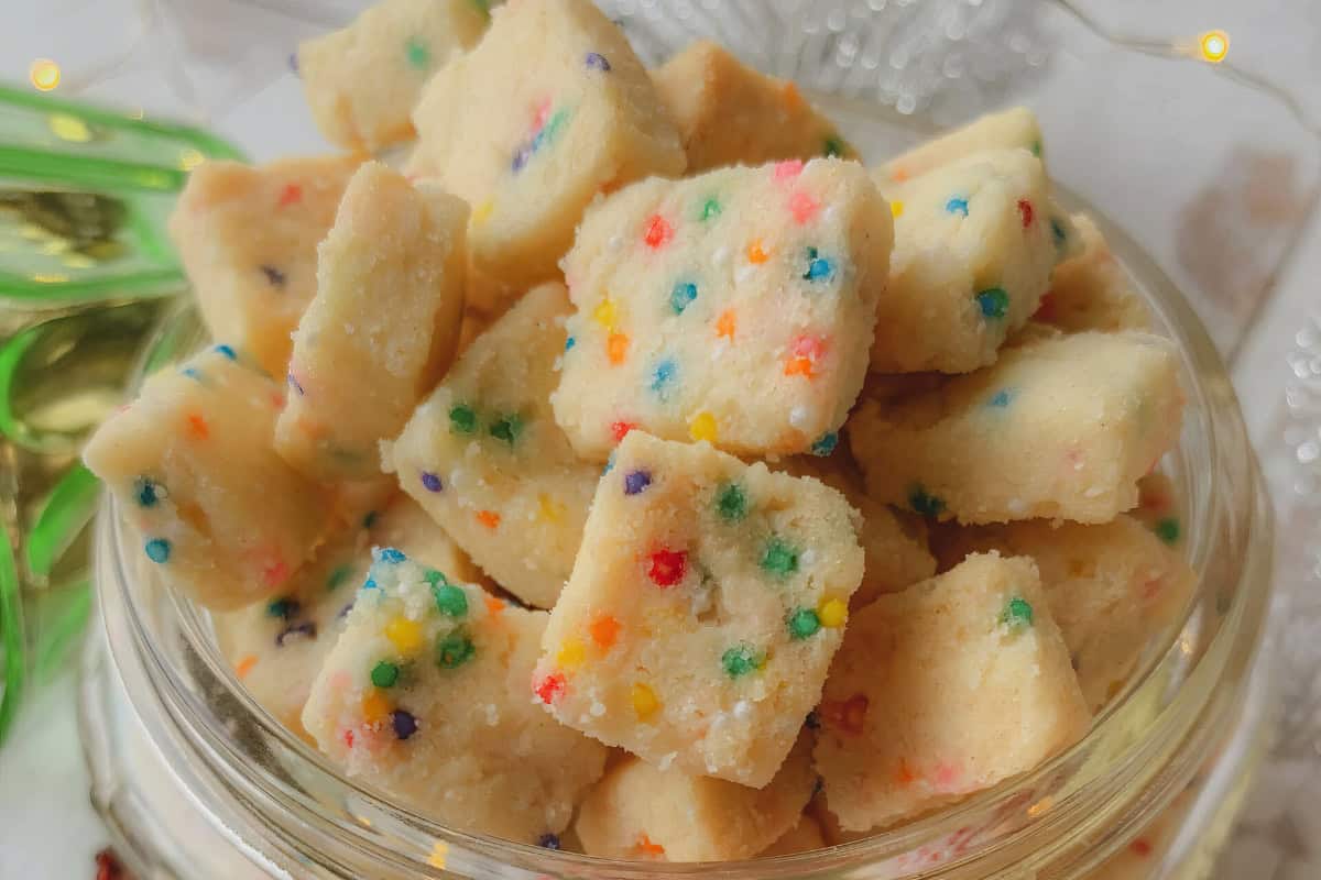 A glass bowl contains vibrant cookie squares topped with sprinkles.